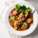 Albondigas soup with Mexican beef meatballs, carrots, zucchini, corn, and onions in tomato broth in a white bowl with cilantro.