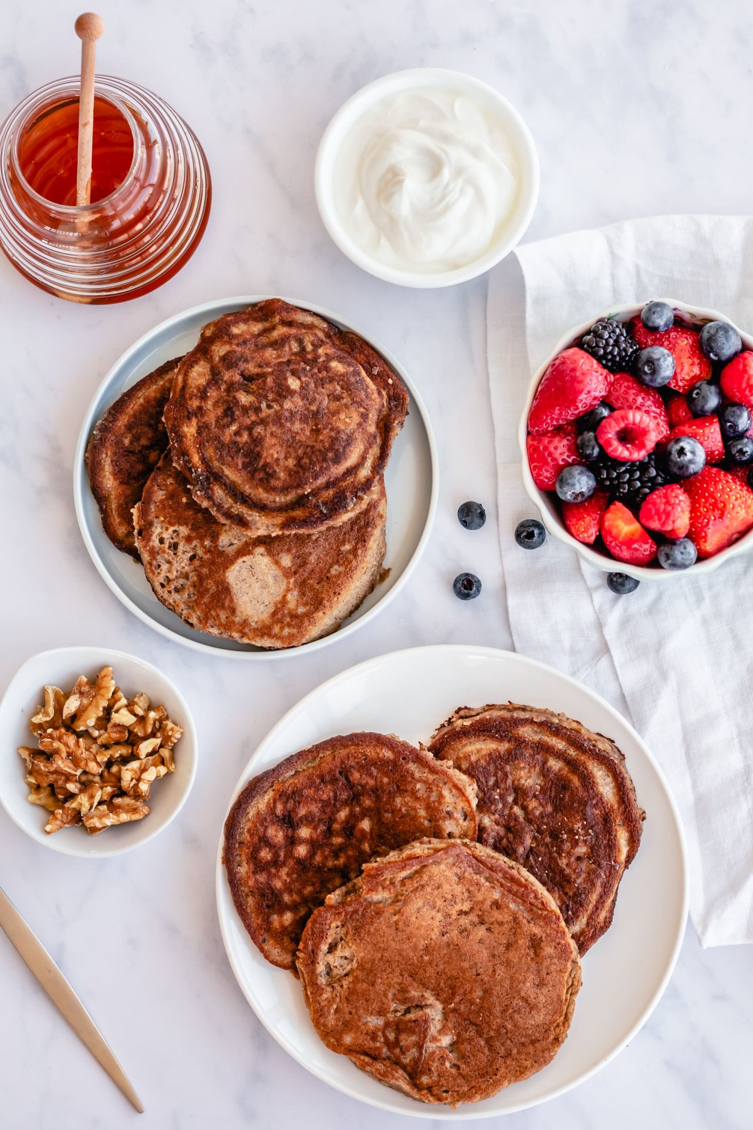 Flax and almond four pancakes on two plates with berries and yogurt on the side.