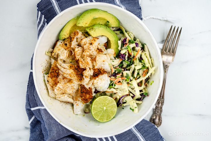 Ancho fish taco bowl with lime slaw and sliced avocado with a blue napkin.