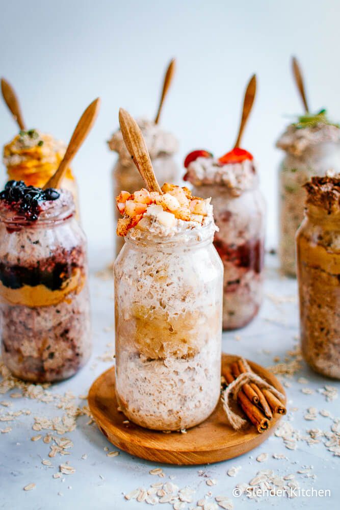 Apple overnight oatmeal in a jar with a wooden spoon with other flavors of oats in the background.