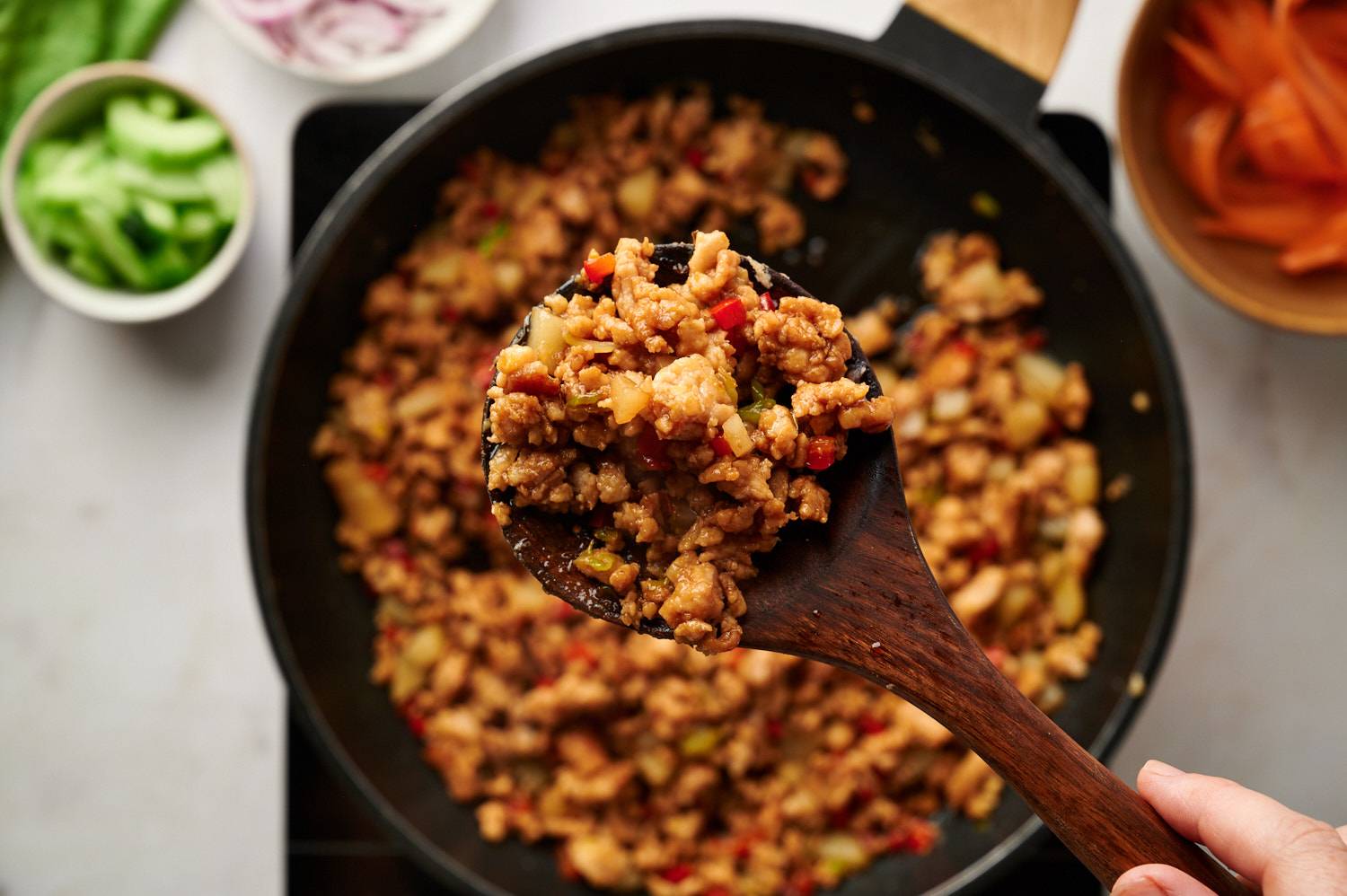 Ground turkey with red bell peppers, water chestnuts, and mushrooms in an Asian sauce on a wooden spoon with a skillet in the background.