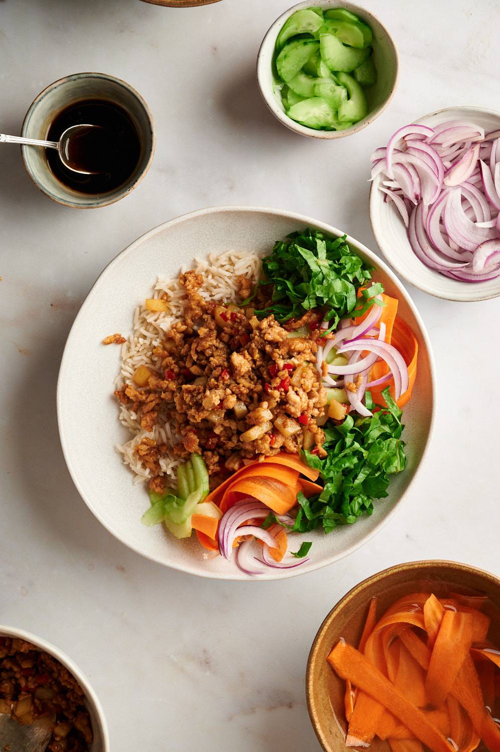 Ground turkey bowls with Asian sauce in a bowl with rice, carrots, lettuce, green onions, and cucumbers.