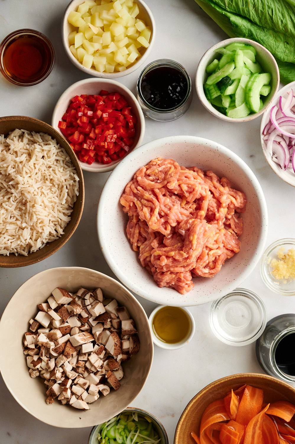 Ingredients for Asian ground turkey bowls including ground turkey, mushrooms, red bell peppers, water chestnuts, hoisin sauce, carrots, onions, and lettuce.