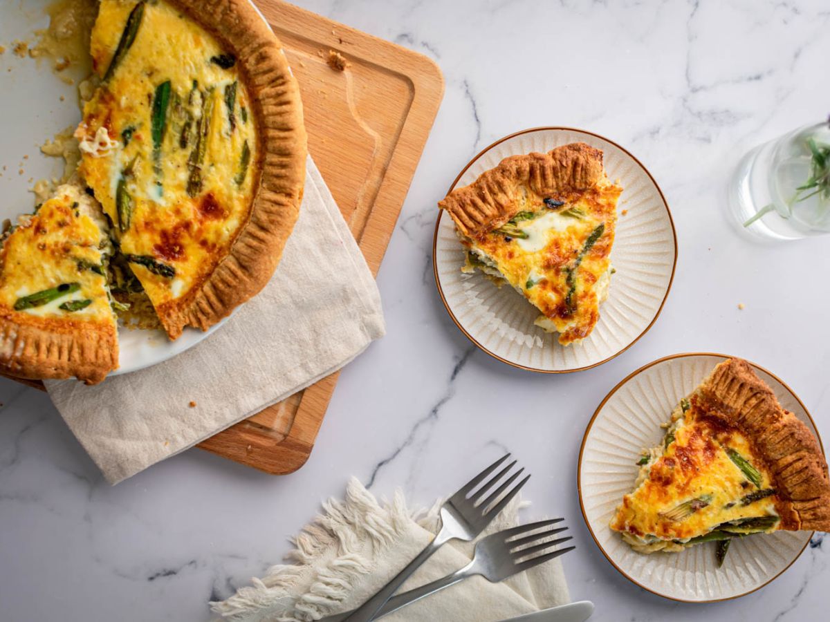 Asparagus quiche with eggs, shredded cheese, asparagus, and red onions cooked in a golden brown crust and served on plates.