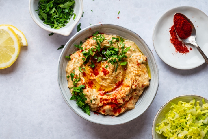 Baba ganoush eggplant dip with tahini, olive oil, and garlic topped with parsley in a bowl.