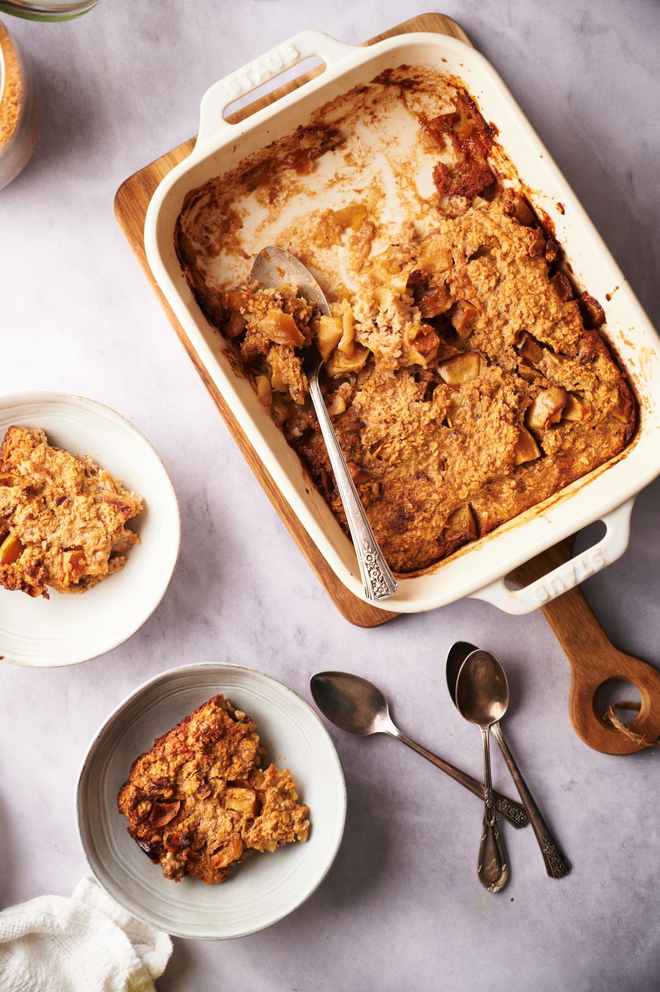 Baked apple oatmeal in a white baking dish and served on two plates. 