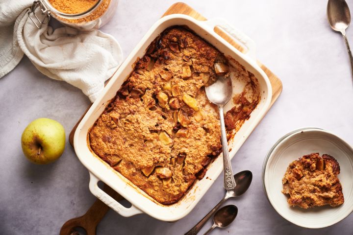 Baked apple cinnamon oatmeal in a baking dish with tender apples and a spoon.