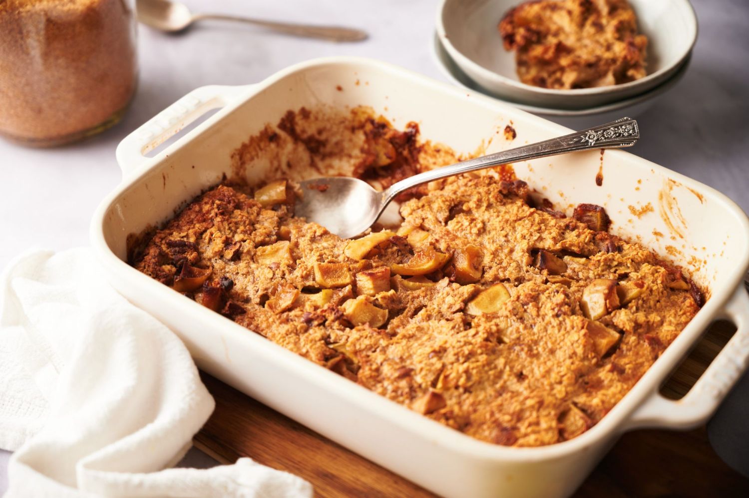 Baked oatmeal with apples and cinnamon in a white baking dish being served with a large spoon.