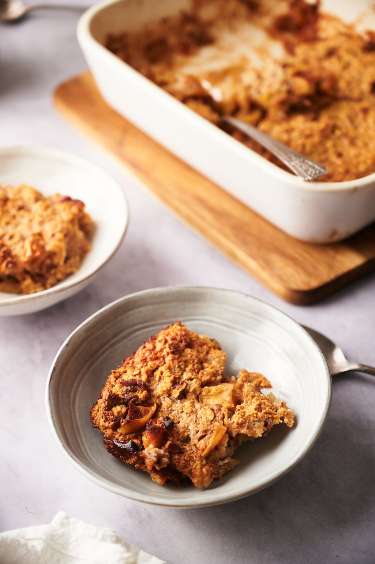 Apple cinnamon baked oatmeal served on a plate and in a large baking dish. 