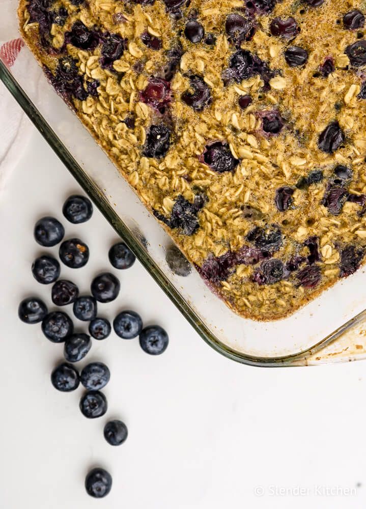 Baked blueberry oatmeal in a glass dish with blueberries on the side.