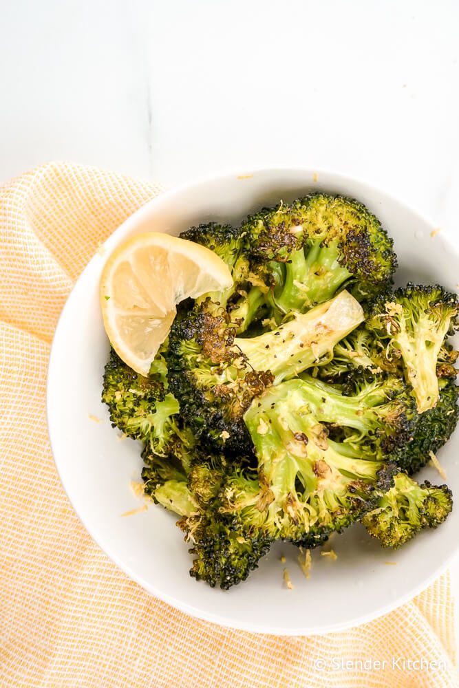 Baked broccoli recipe in a white bowl with lemon zest and garlic.