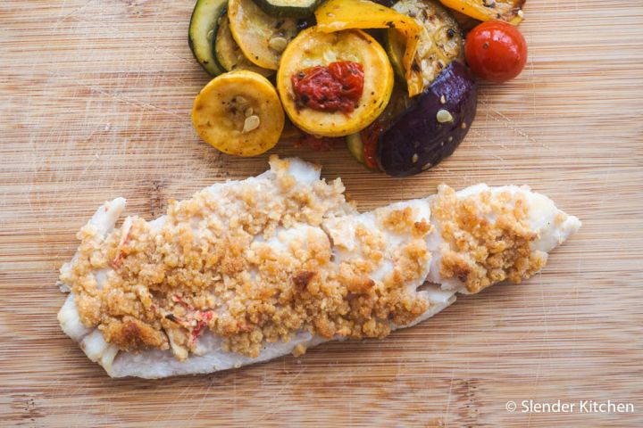 Baked haddock with seafood stuffing and vegetables on a cutting board.