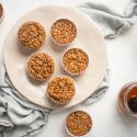 Baked oatmeal muffins with bananas served on a plate with raspberries and maple syrup on the side.