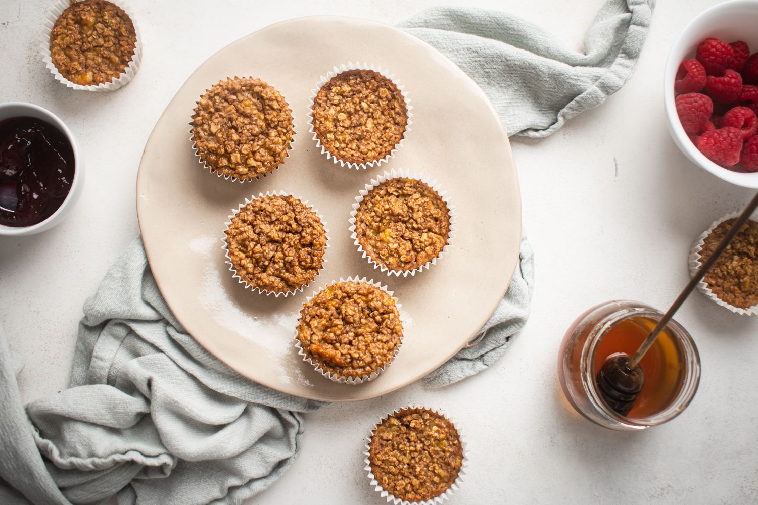 Baked oatmeal muffins with bananas served on a plate with raspberries and maple syrup on the side.