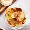 Baked potato chips on parchment paper with with parsley and dipping sauce.