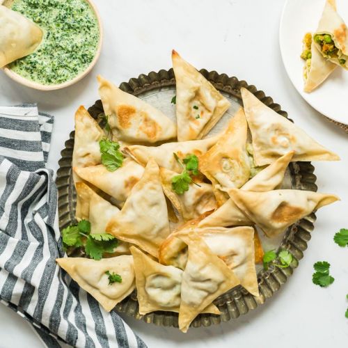 Baked samosa filled with potato, cauliflower, and peas on a plate with cilantro and mint dipping sauce.