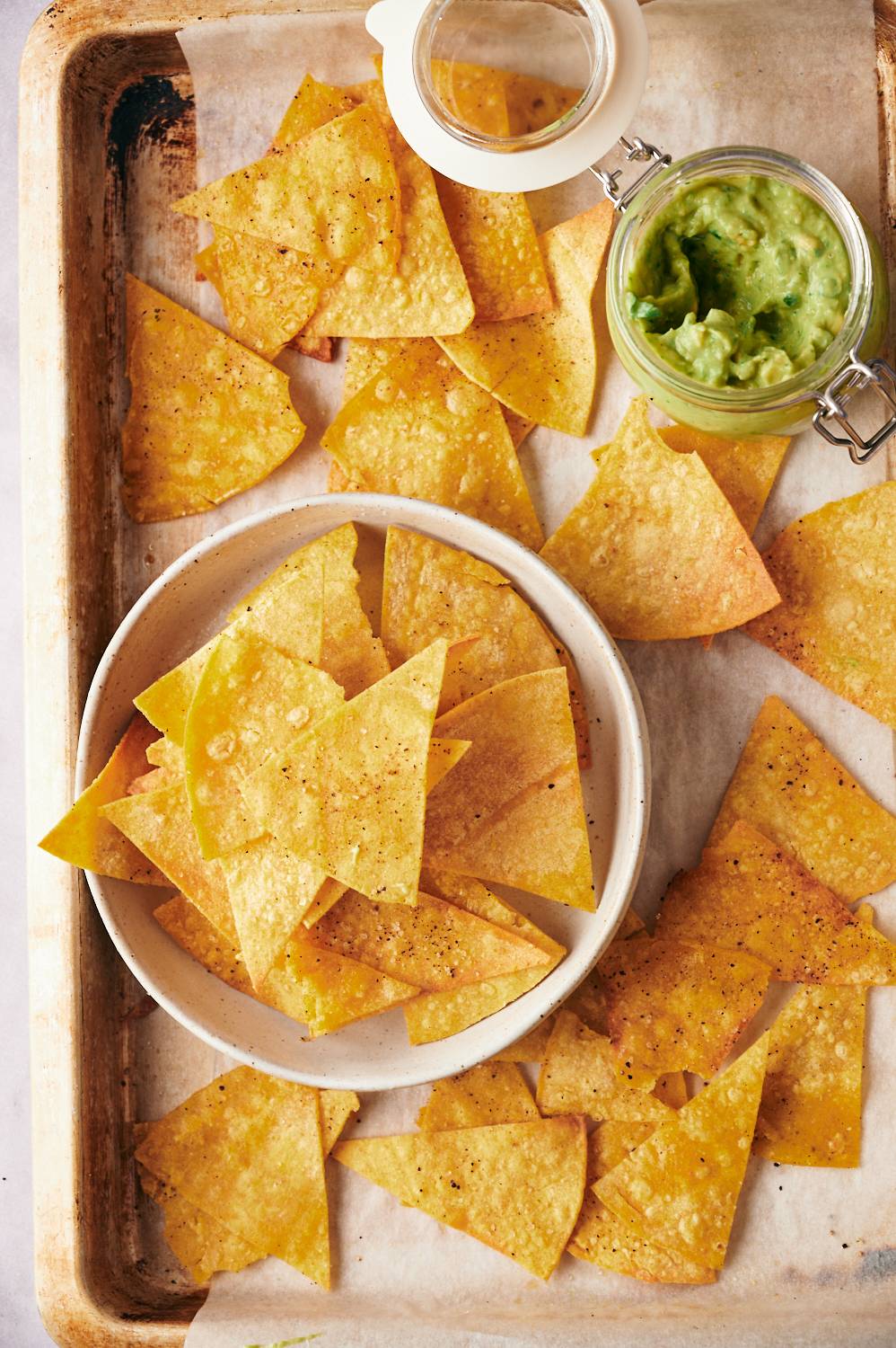 Baked corn tortilla chips with sea salt and chili powder served on a sheet pan with guacamole.