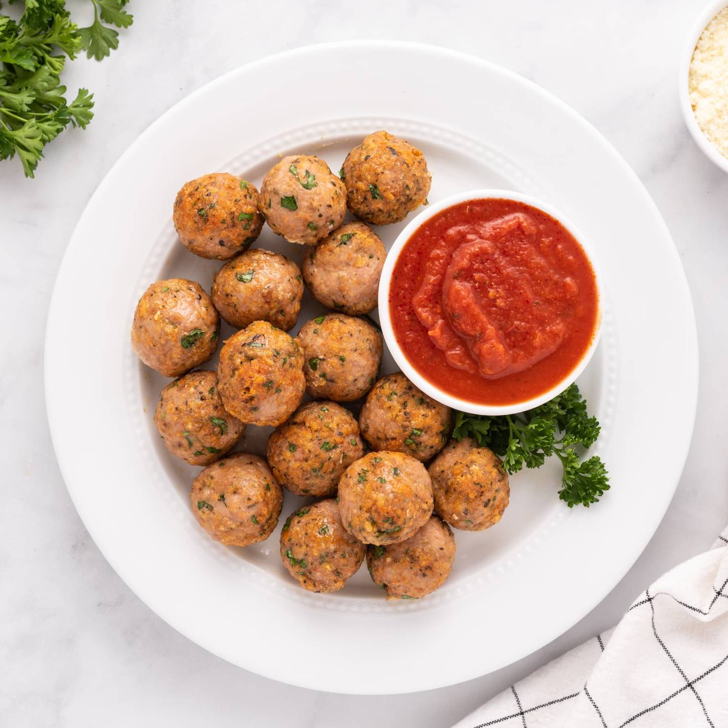 Baked turkey meatballs with parsley and Parmesan cheese on a plate with marinara sauce.