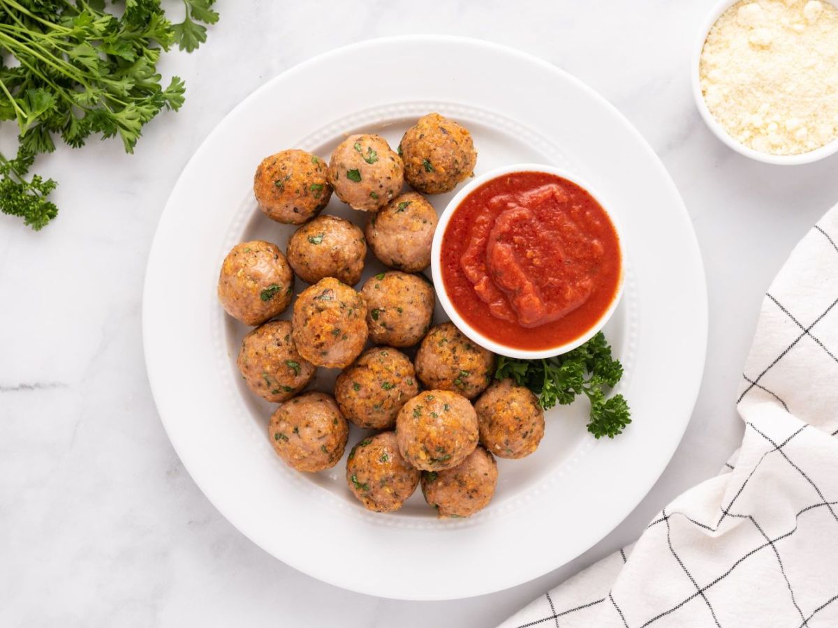 Baked turkey meatballs with parsley and Parmesan cheese on a plate with marinara sauce.