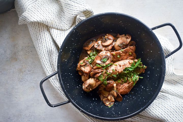 Balsamic chicken and mushrooms with fresh thyme and parsley in a bowl with a white napkin.