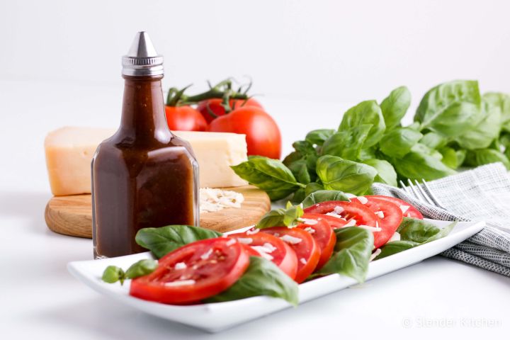 Balsamic vinaigrette in a glass jar with a tomato and basil salad.