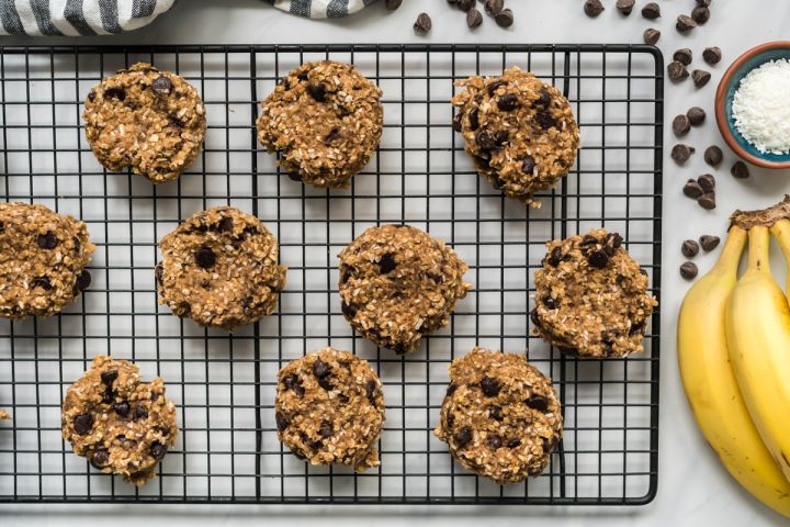 Banana chocolate oat cookies on a wire rack with bananas and dark chocolate chips on the side.