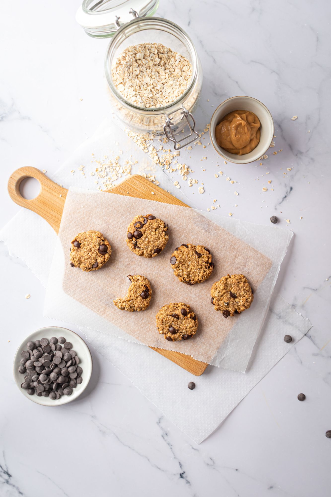 Oatmeal and banana cookies with chocolate chips on a wooden board with peanut butter on the side.