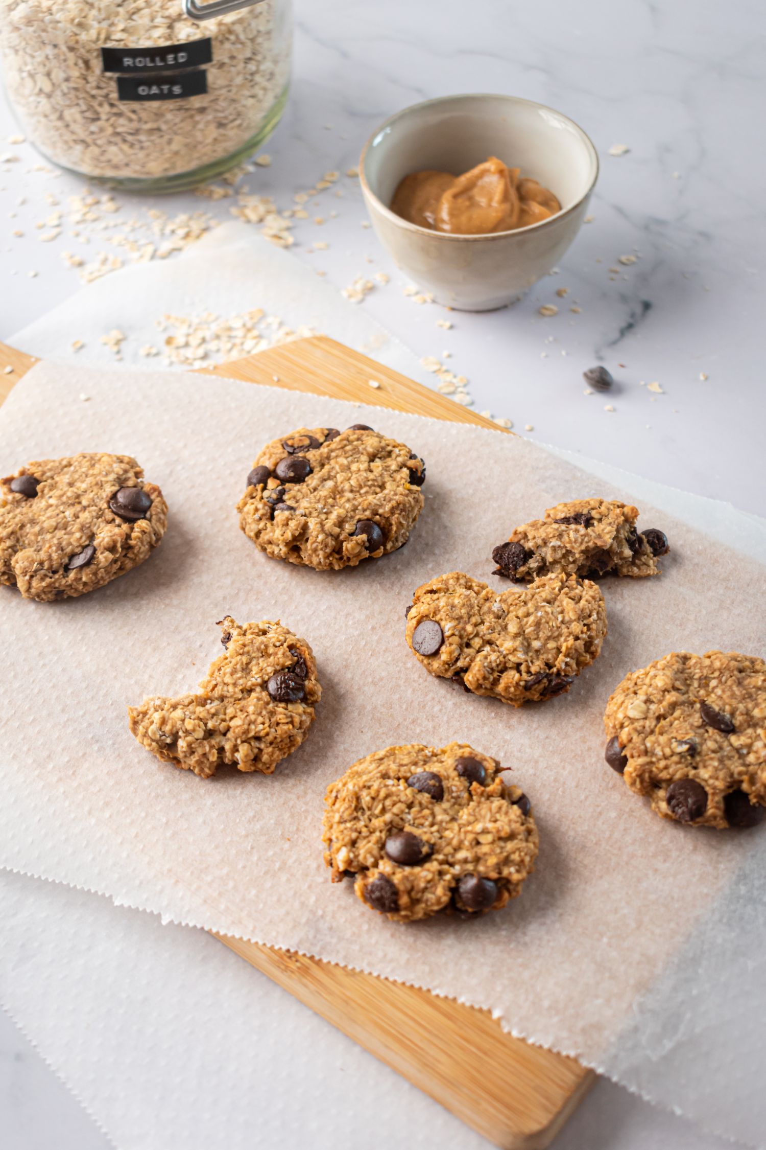 Banana, chocolate chip, and oatmeal cookies on parchment paper and a wooden cutting board.