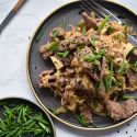 Beef and cabbage stir fry with garlic, green onions, and sesame seeds on a plate with chopsticks.