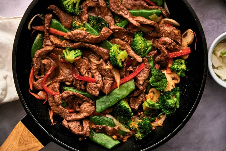 Beef stir fry with tender strips of beef with broccoli, carrots, bell peppers, and snow peas in soy stir fry sauce in a skillet.