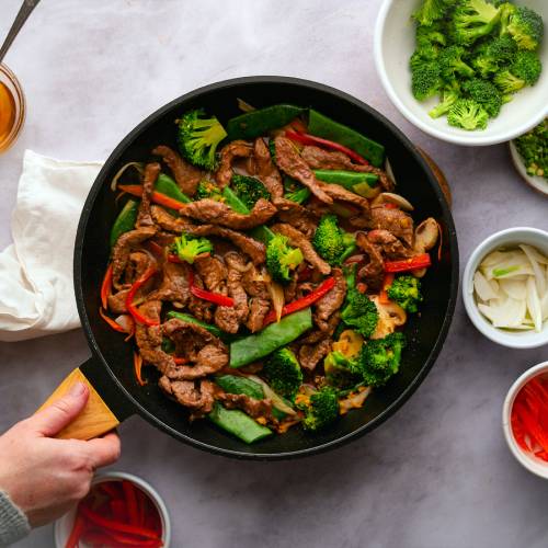 Beef stir fry with tender strips of beef with broccoli, carrots, bell peppers, and snow peas in soy stir fry sauce in a skillet.