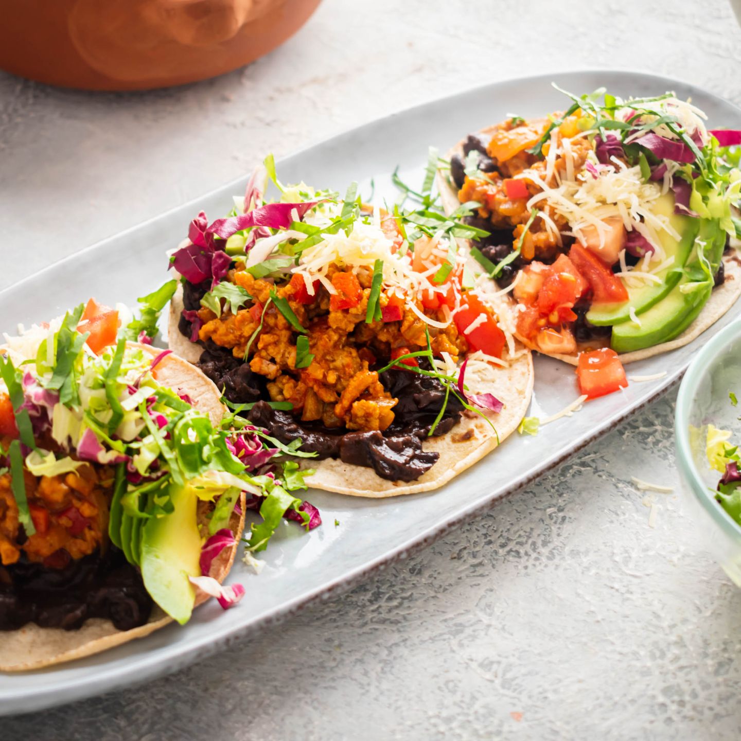 Beef tostadas with ground beef, refried beans, avocado, salsa, lettuce, tomato, and cheese on a plate.