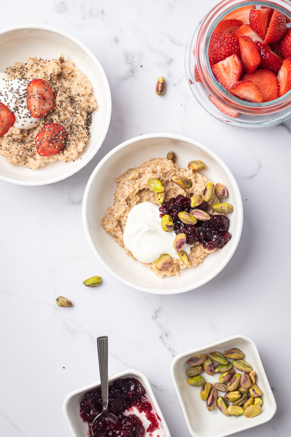 Microwave rolled oats in two bowls with strawberries, chia seeds, jam, Greek yogurt, and pistachios.