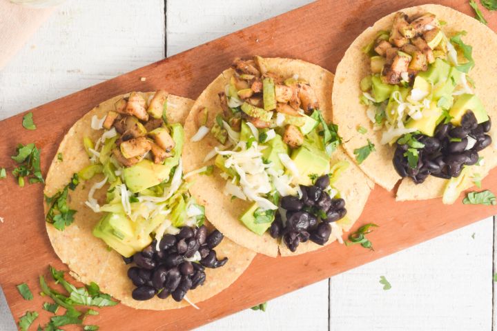 Black bean and zucchini tacos with avocado and cabbage slaw on corn tortillas.