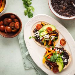 Black bean tostadas served on crispy baked tostada shells with peppers, onions, avocado, cheese, and tomatoes.