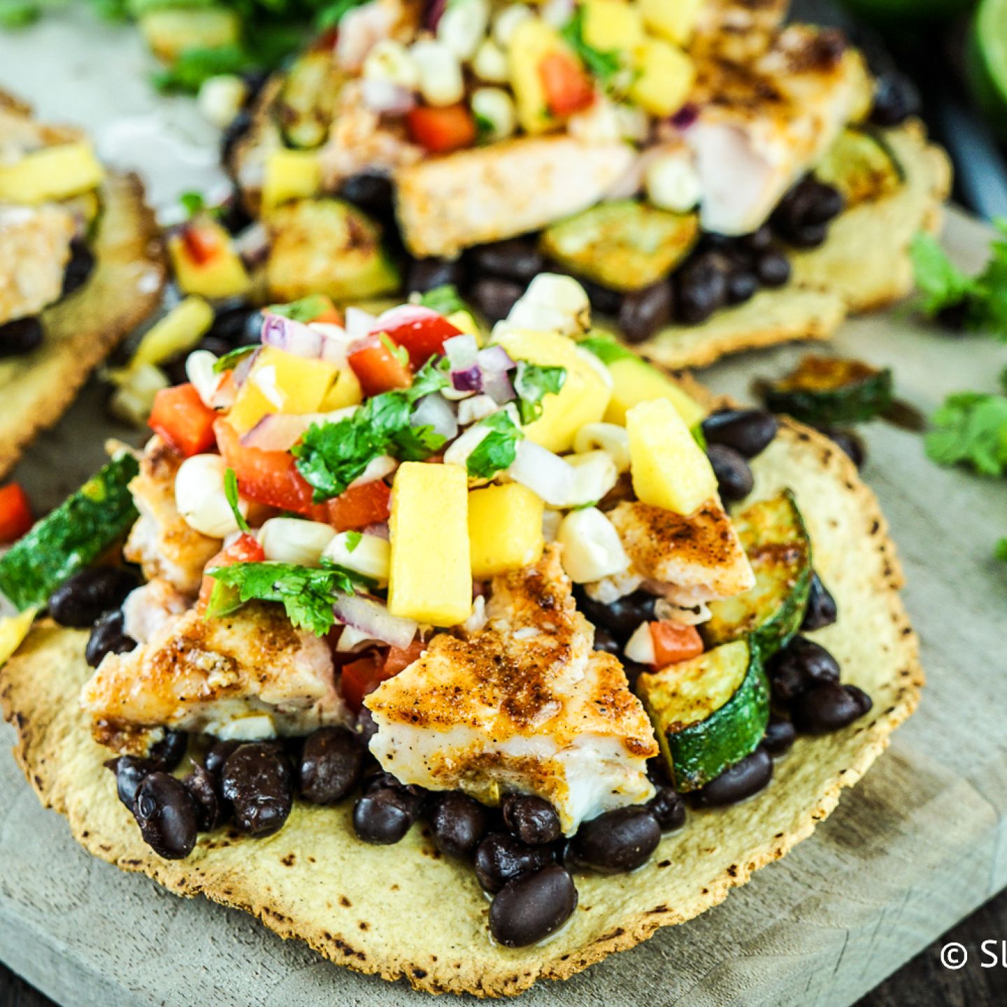 Salmon tostadas with blackened salmon, zucchini, veggies, and cheese on a crispy tortilla.