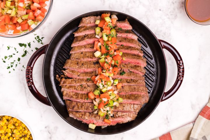 Marinated flank steak served with a tomato, celery, and onion salsa on a grill pan.