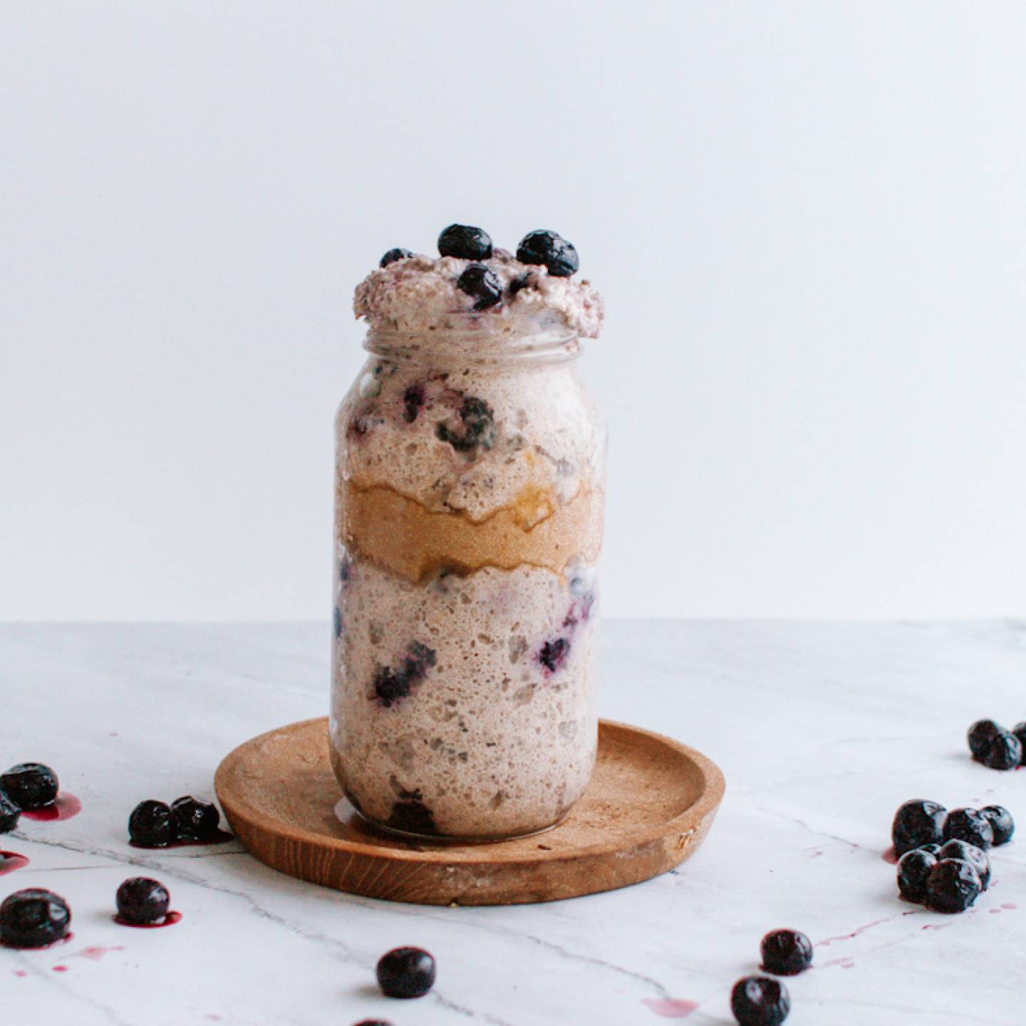 Blueberry overnight oatmeal with almond butter in a mason jar with blueberries on the side.