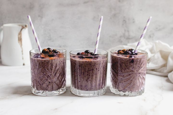 Blueberry banana smoothie with frozen bananas, blueberries, and spinach blended in a glass with blueberries on top. 