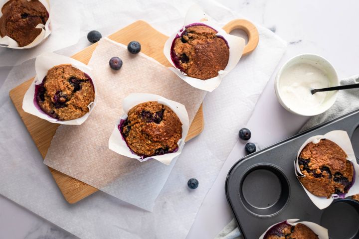 Blueberry oatmeal muffins with fresh blueberries in parchment paper on a cutting board.