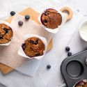 Blueberry oatmeal muffins with fresh blueberries in parchment paper on a cutting board.