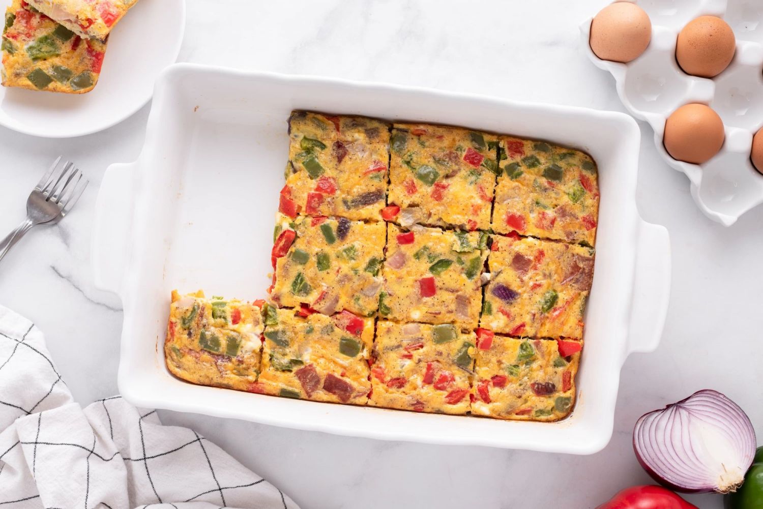 Healthy egg casserole with vegetables, bacon, and cheese cut into slices in a baking dish.