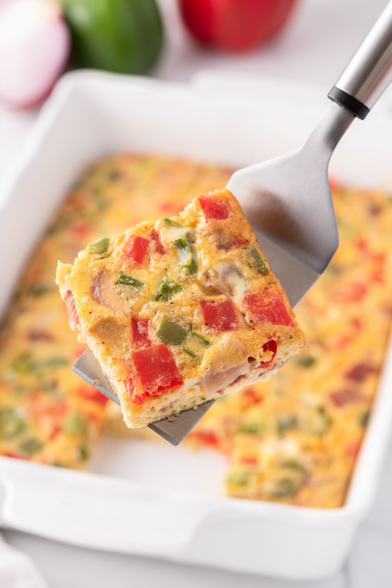 Bacon egg casserole being lifted on a spatula with peppers, onions, eggs, and cheese.