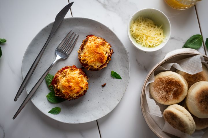 Breakfast English muffin pizzas with eggs, tomato sauce, basil, and melted cheese on a plate with English muffins on the side.