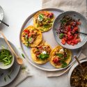 Breakfast tacos with eggs, bacon, and potatoes served in corn tortillas with salsa, sour cream, cilantro, and green onions.