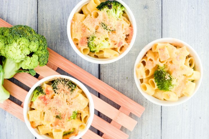 Broccoli macaroni and cheese in three ramekins with a wooden cutting board.