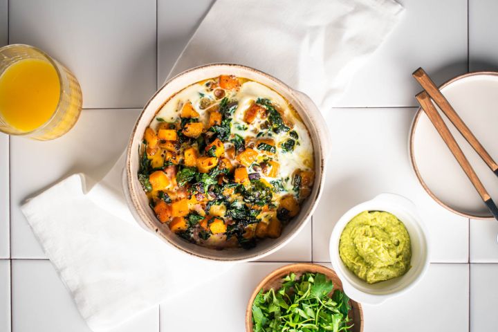 Butternut squash and egg breakfast casserole with turkey sausage in a baking dish with avocado on the side.