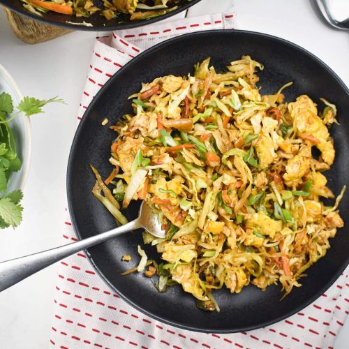 Cabbage fried rice with shredded cabbage, carrots, green onions, eggs, and soy sauce on a black plate.