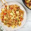 Cauliflower fried rice with cabbage, carrots, eggs, and green onions on a plate with chopsticks.