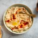 Cauliflower hummus with roasted cauliflower, tahini, olive oil, and lemon served in a bowl with breadsticks on the side.